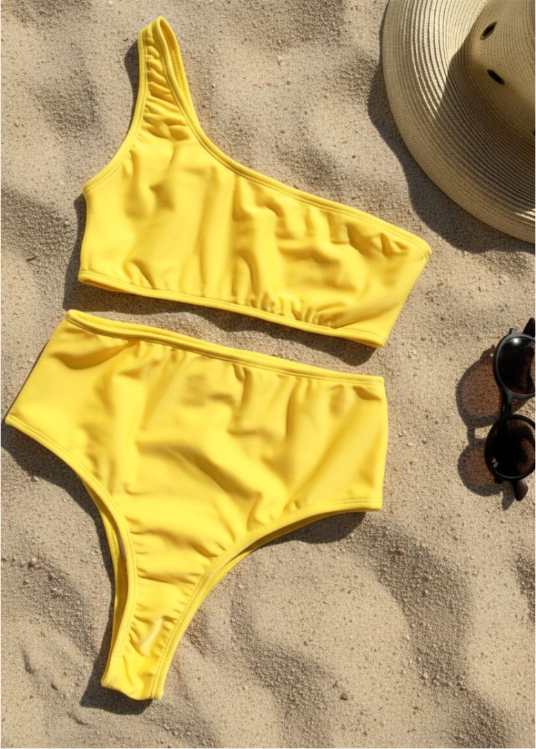 Bikini de mujer con top asimétrico y braga alta en color amarillo - vista de frente apoyado sobre la arena